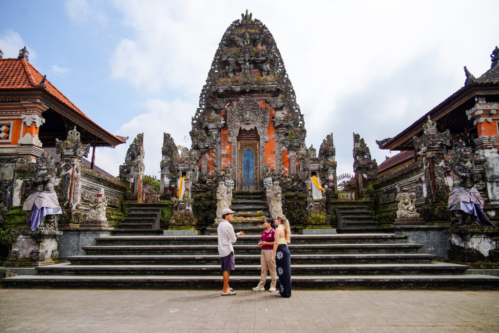 Guests visiting a traditional Balinese temple, standing at the grand entrance surrounded by intricate stone carvings and rich cultural heritage in Bali.