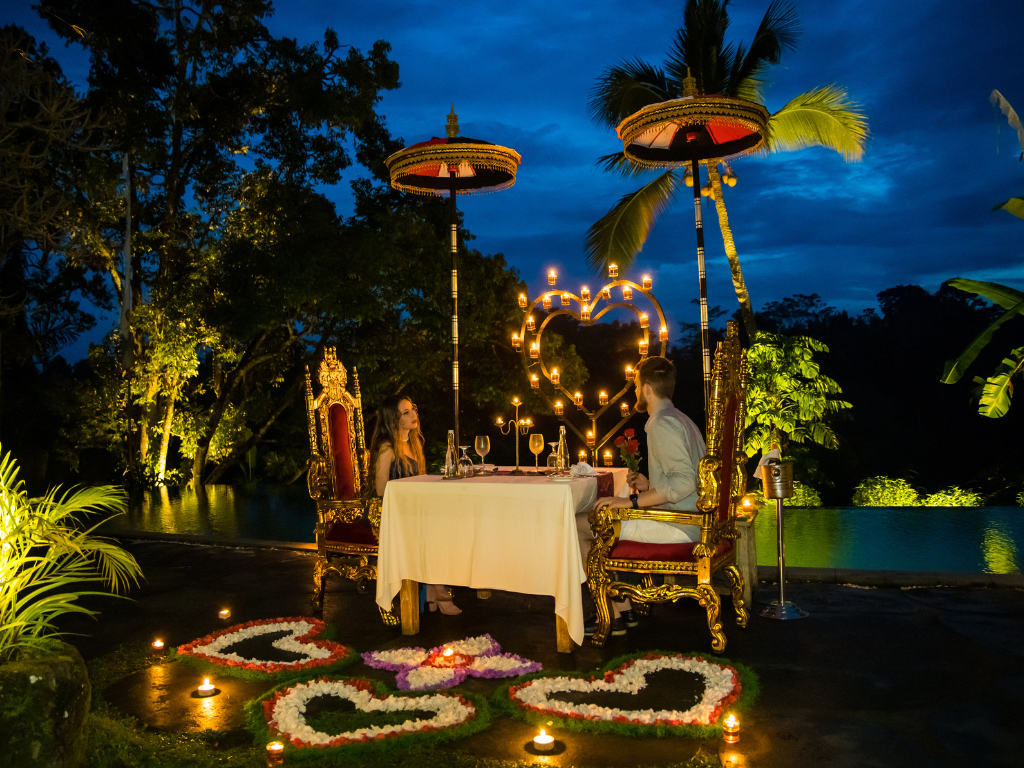 Romantic candlelight dinner setup in a tropical garden with traditional Balinese umbrella decor at night.
