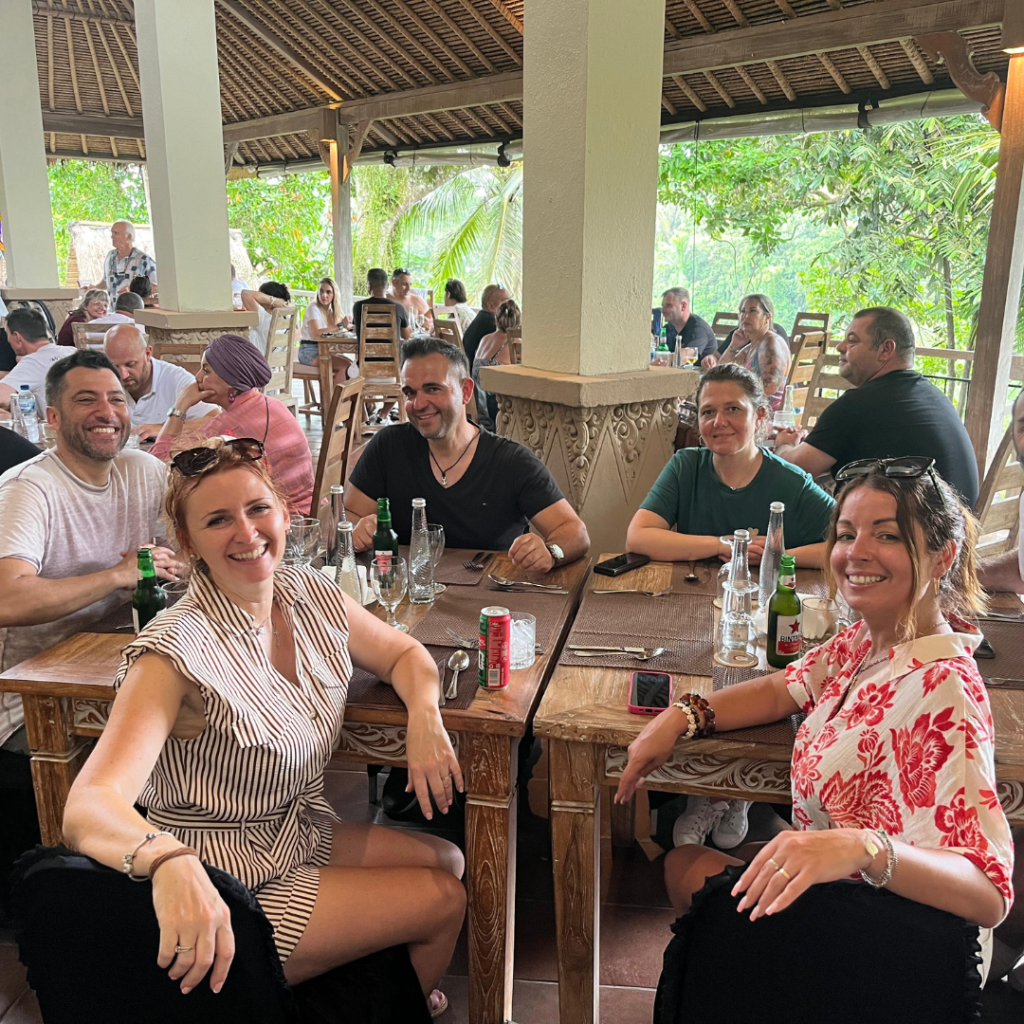 Group of guests enjoying a casual gathering and conversation at an open-air tropical lounge surrounded by lush greenery in Bali.